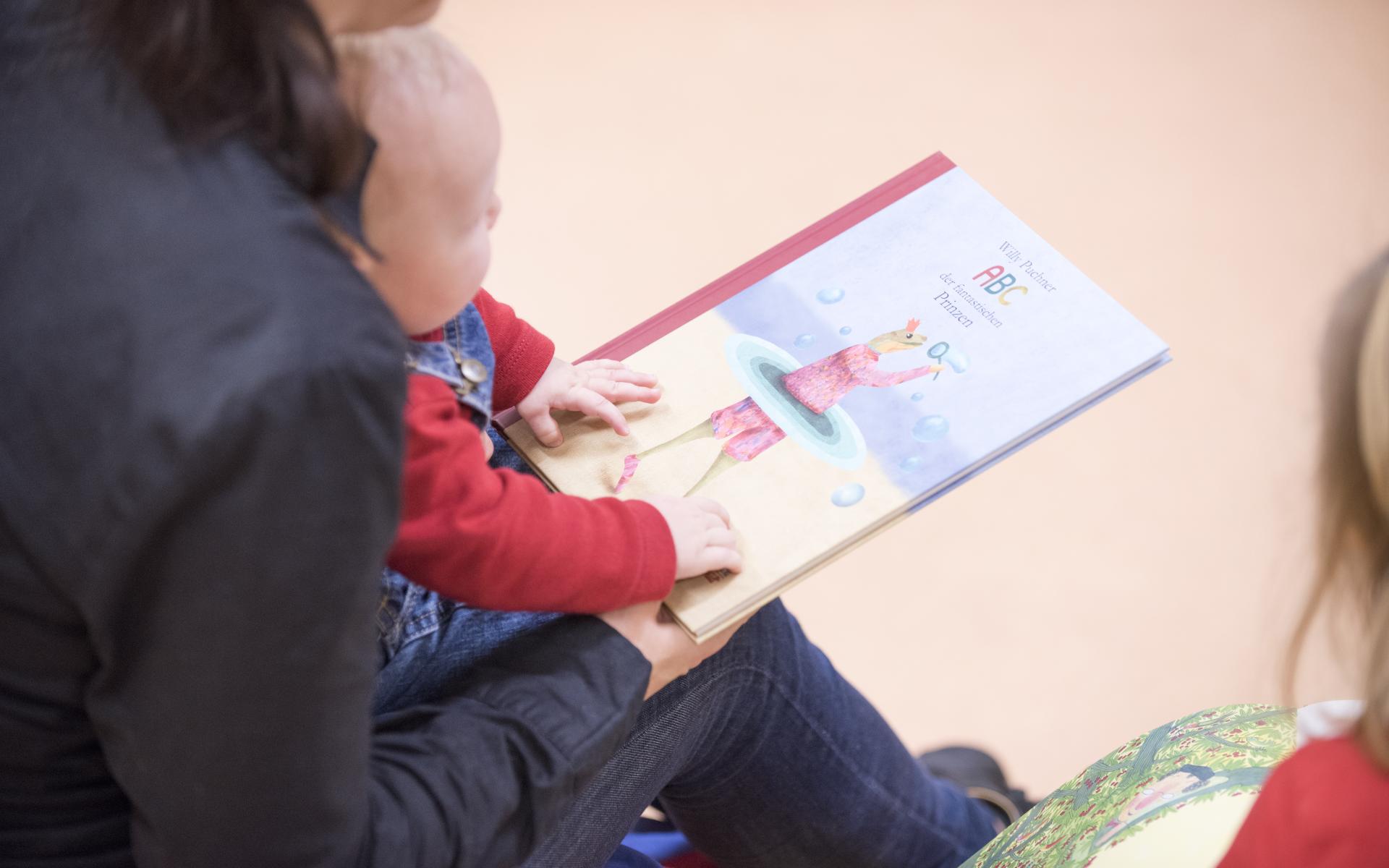 Mutter mit Kleinkind am Schoß beim Buchdurchblättern