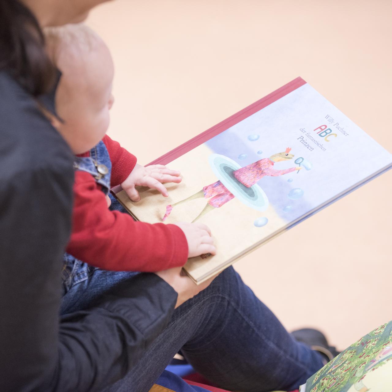 Mutter mit Kleinkind am Schoß beim Buchdurchblättern